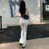 A woman in white flare jeans and tank top stands near a tiled wall, showing back view of the outfit with a black shoulder bag