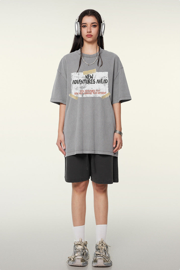 Woman wearing gray oversized t-shirt with "New Adventures Ahead" graphic print, dark shorts and silver headphones