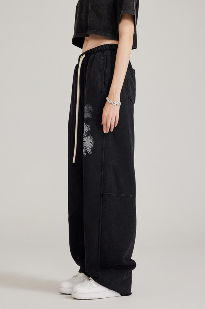 Side profile of model in black two-piece set with oversized sweatpants featuring graphic detail and chain bracelet