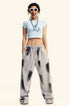 Model in a light blue graphic crop top and gray sweatpants, posing with sunglasses and a statement necklace