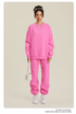 Model in bright pink sweatsuit with white bag, sneakers and silver necklace on neutral background