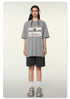 Full body shot of woman in gray graphic t-shirt with adventure slogan, black shorts, white socks and chunky sneakers