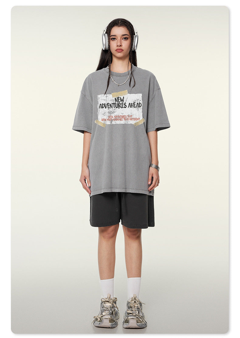 Full body shot of woman in gray graphic t-shirt with adventure slogan, black shorts, white socks and chunky sneakers