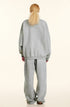 Back view of blonde model with half-up hairstyle wearing light gray sweatshirt and matching pants, slouchy oversized silhouette, white background