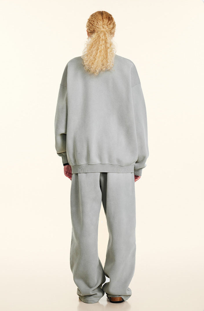 Back view of blonde model with half-up hairstyle wearing light gray sweatshirt and matching pants, slouchy oversized silhouette, white background