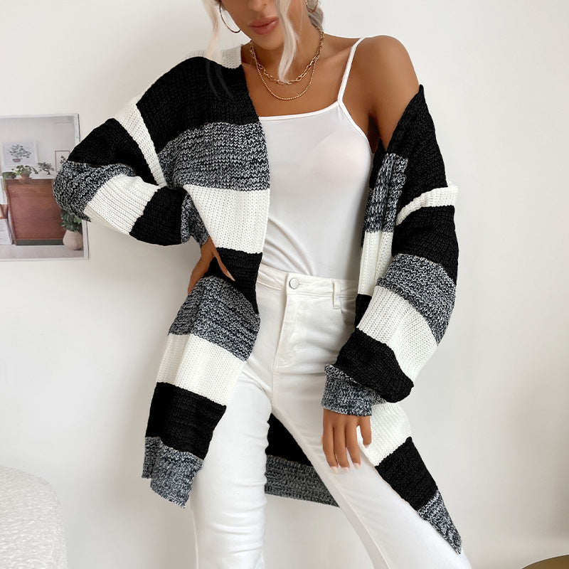 A woman in black, white and gray striped open cardigan with white camisole and white jeans shown against clean white background