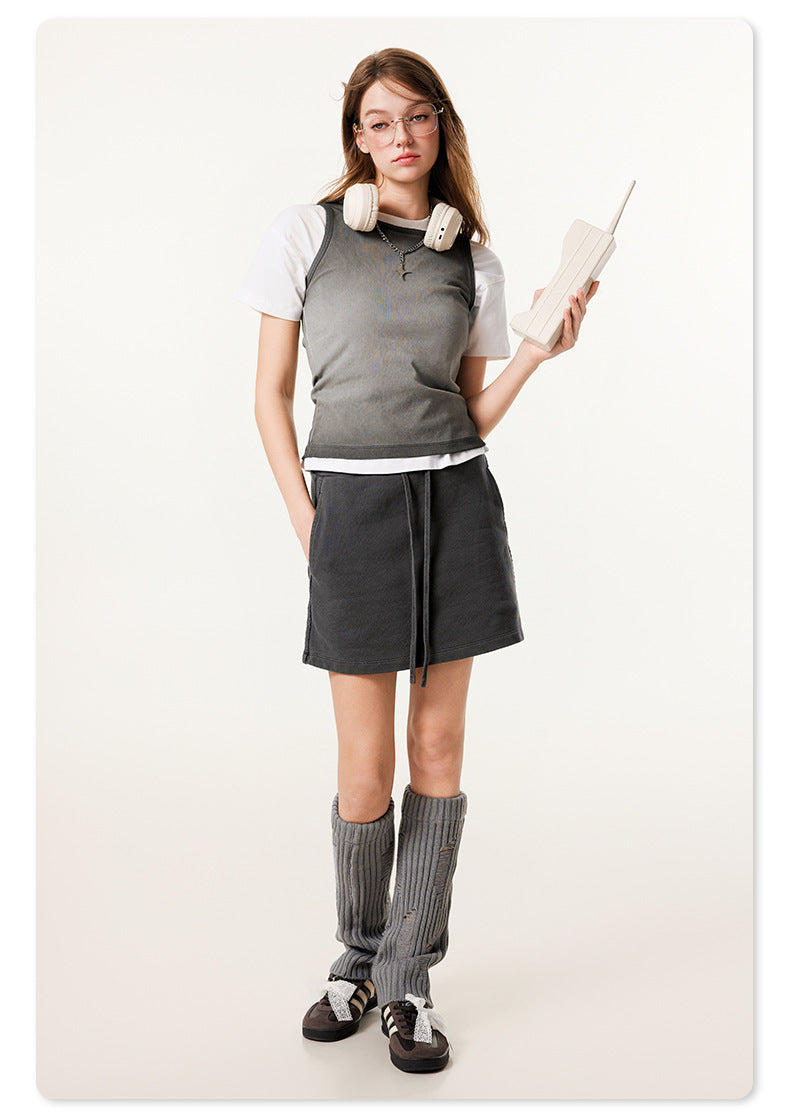 Model wearing black mini skirt with white headphones, tank top and cream leg warmers, holding vintage-style phone
