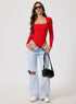 Woman wearing a red bodysuit and light blue jeans with a black handbag on a white background