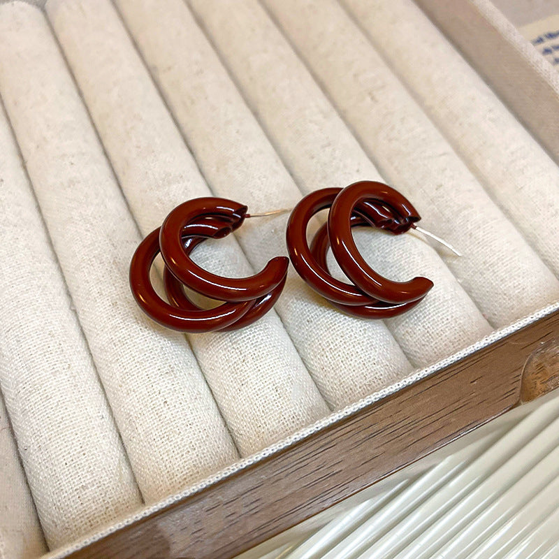 A pair of gold hoop earrings with large red matte spheres, placed on a cushioned jewelry box
