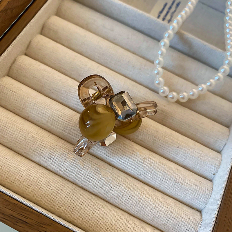 A mini brown resin hair claw adorned with crystal embellishments, placed in a cushioned jewelry tray.