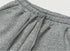 A close-up of gray sweatpants showcasing the elastic waistband with adjustable drawstrings, highlighting the ribbed fabric texture