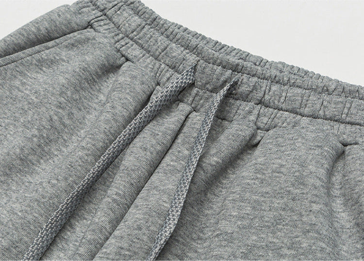A close-up of gray sweatpants showcasing the elastic waistband with adjustable drawstrings, highlighting the ribbed fabric texture