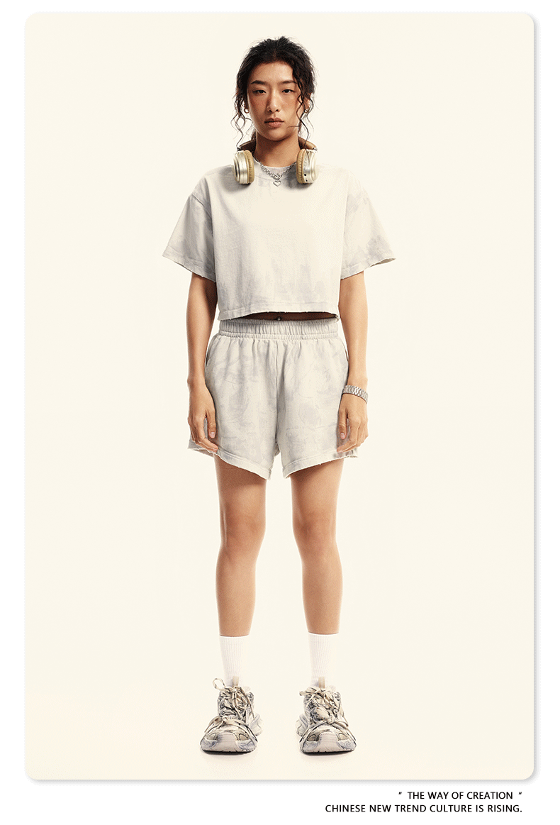 Model in off-white cropped tee and matching shorts with elastic waist, white socks and gray sneakers