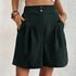 Model wearing dark green pleated shorts with dual button closure and side pockets, paired with white crop top