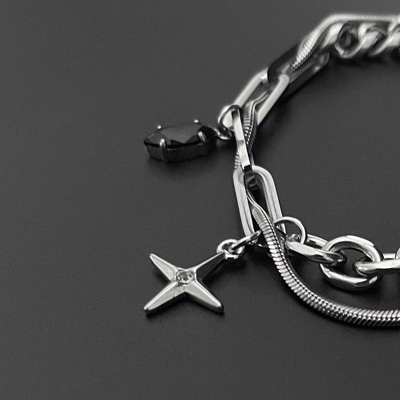 Close-up of silver chain bracelet with cross pendant and black gemstone charm on a sleek black background, showcasing intricate details.