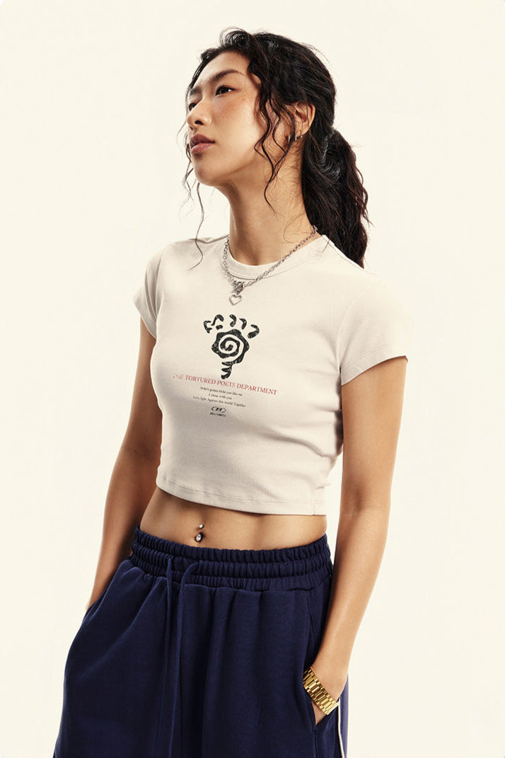 Model wears a white cropped T-shirt with a graphic print and navy sweatpants, styled with a silver chain necklace