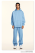 Model in light blue hoodie and sweatpants set with white headphones and silver chain on neutral background