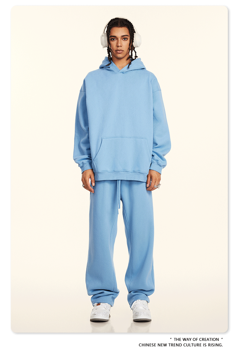 Model in light blue hoodie and sweatpants set with white headphones and silver chain on neutral background