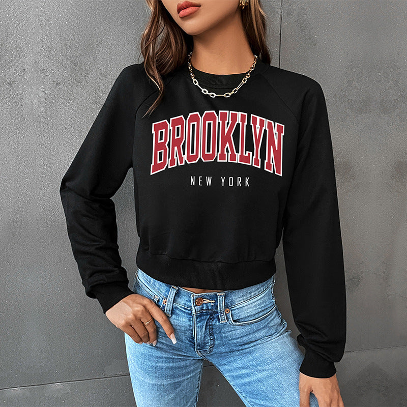 Trendy black cropped sweatshirt with Brooklyn graphic text in red, paired with light wash jeans and chain necklace