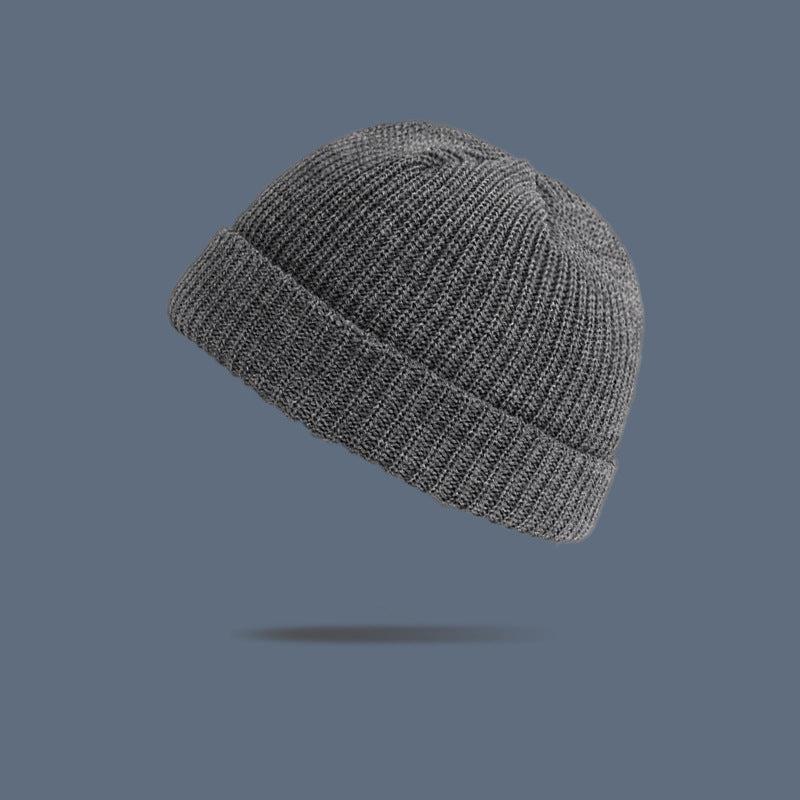 A heather gray ribbed knit beanie with folded cuff floating against slate gray background, showing versatile winter hat style