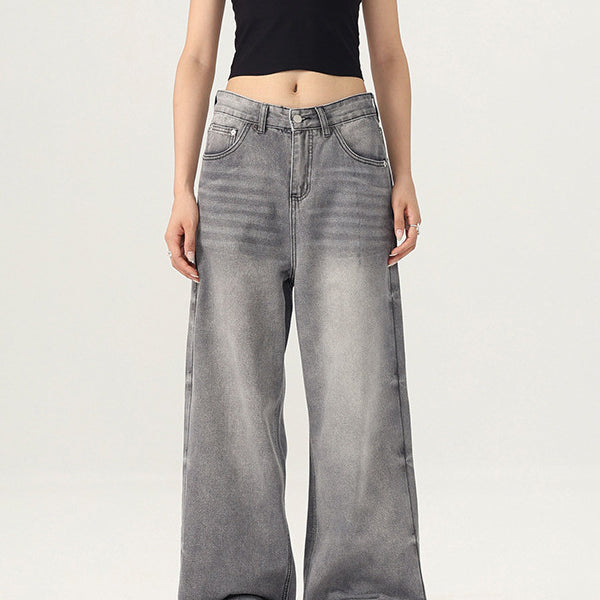 A woman wearing a black crop tank top and gray wide-leg jeans stands against a white background