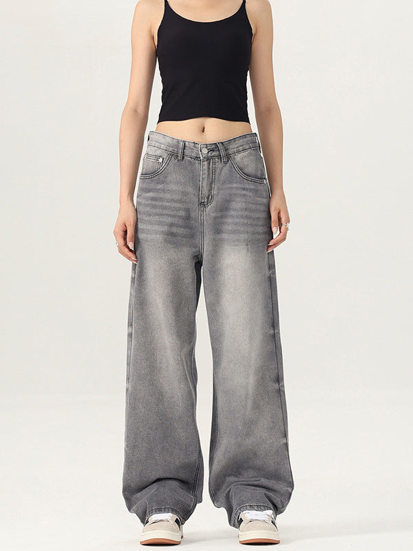 A woman wearing a black crop tank top and gray wide-leg jeans stands against a white background