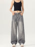 A woman posing with hands in pockets, wearing black crop tank and gray wide-leg denim jeans against white backdrop