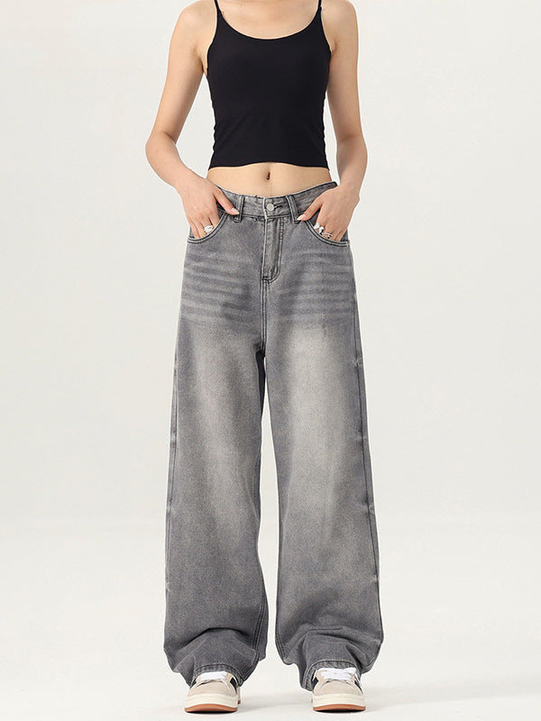 A woman posing with hands in pockets, wearing black crop tank and gray wide-leg denim jeans against white backdrop