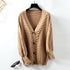 Beige chunky knit cardigan with cable pattern and button front displayed on hanger, styled with black sunglasses