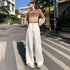 A woman is posing on a crosswalk wearing a beige cropped sweater with text, white high-waisted wide-leg pants and beige sneakers