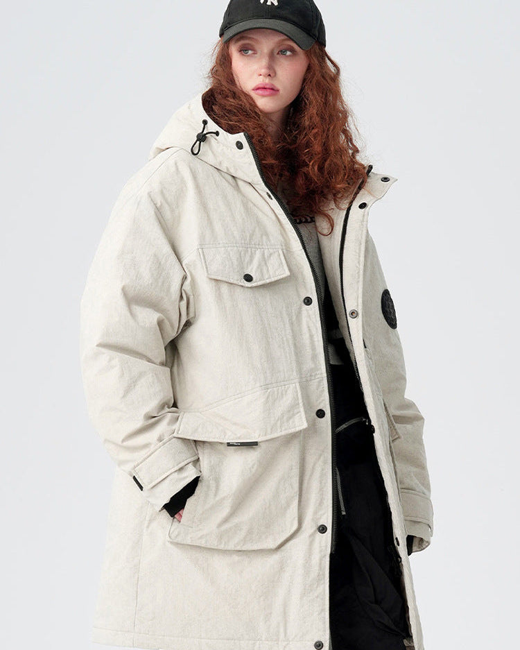 A woman with curly red hair wearing NY cap and cream-colored Be_Born parka with utility pockets poses against white background