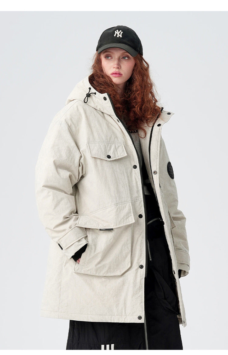A woman with curly red hair wearing NY cap and cream-colored Be_Born parka with utility pockets poses against white background