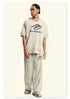 Model wearing cream Backstairs oversized t-shirt and wide-leg sweatpants with distressed effects, silver chain necklace, and white athletic shoes against white background