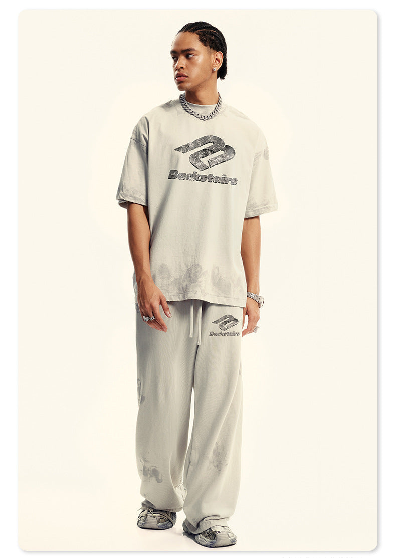 Model wearing cream Backstairs oversized t-shirt and wide-leg sweatpants with distressed effects, silver chain necklace, and white athletic shoes against white background