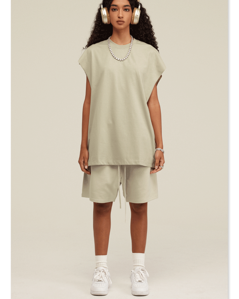Model wearing cream-colored oversized muscle tee and matching shorts with white headphones and pearl necklace