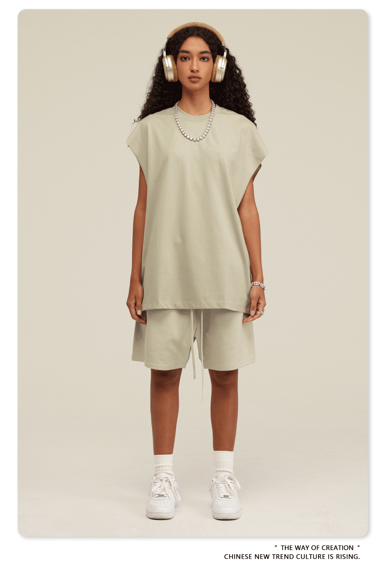 Model wearing cream-colored oversized muscle tee and matching shorts with white headphones and pearl necklace