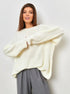 Woman in cream colored chunky knit sweater with grey pleated pants and white sneakers, full length shot