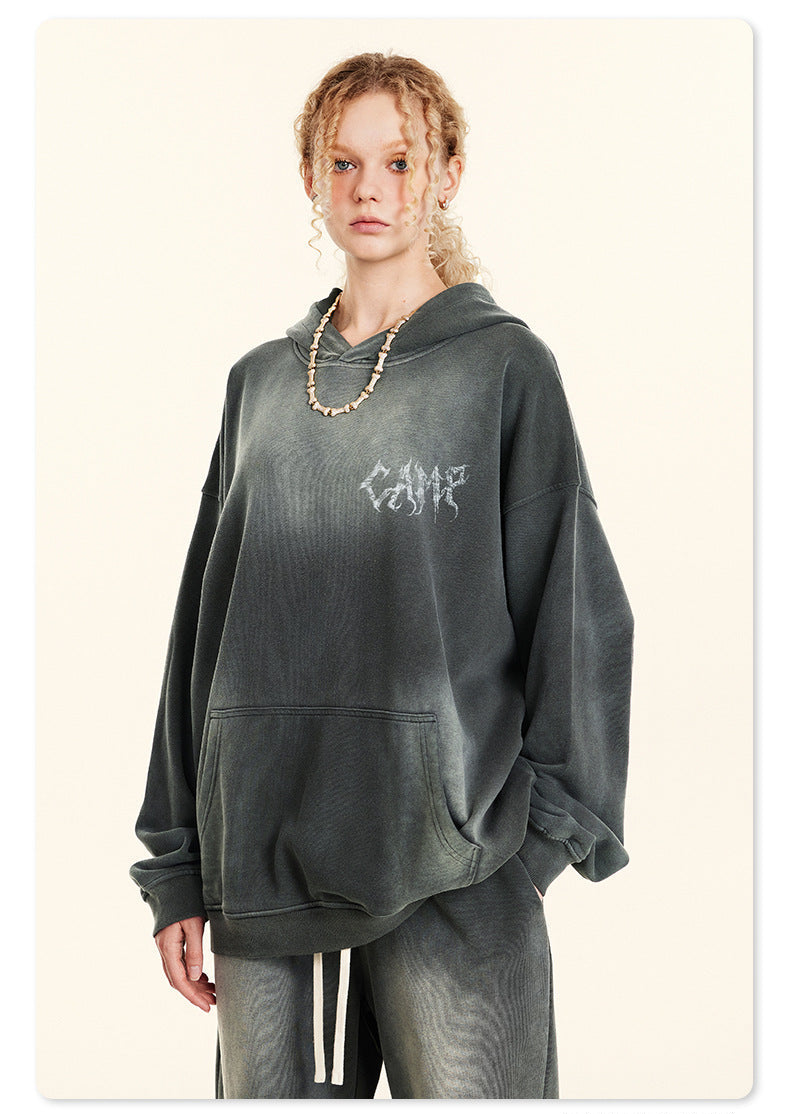 Woman with curly hair in gray washed hoodie with front pocket and small chest logo, wearing matching pants