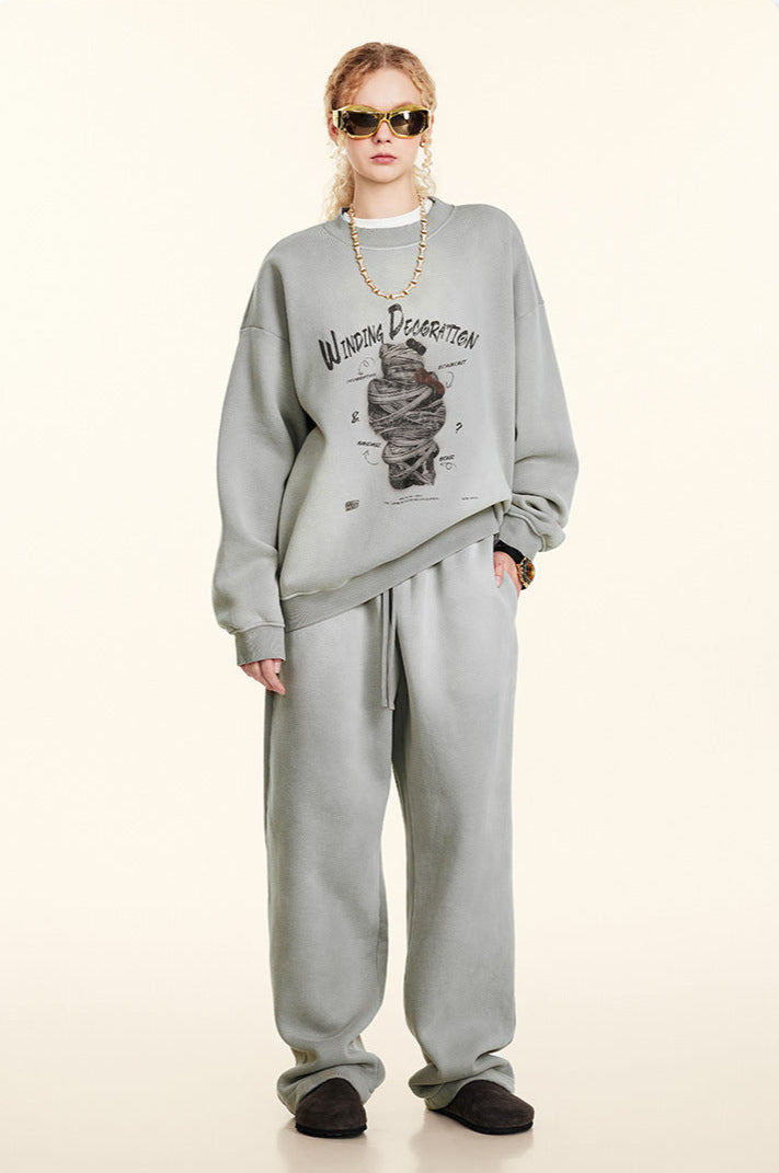 Front view of blonde model in light gray Winding Decoration sweatshirt, matching pants, gold sunglasses, gold chain necklace, dark slippers