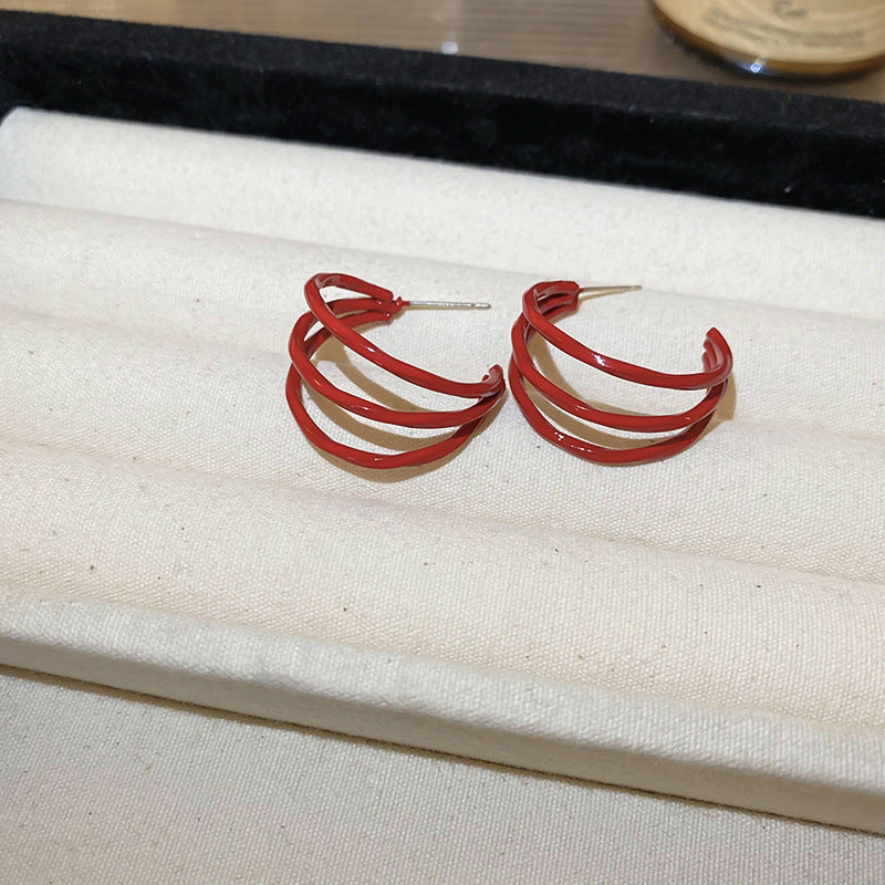 A pair of large gold hoop earrings with a wavy red enamel design, resting on a beige fabric jewelry case