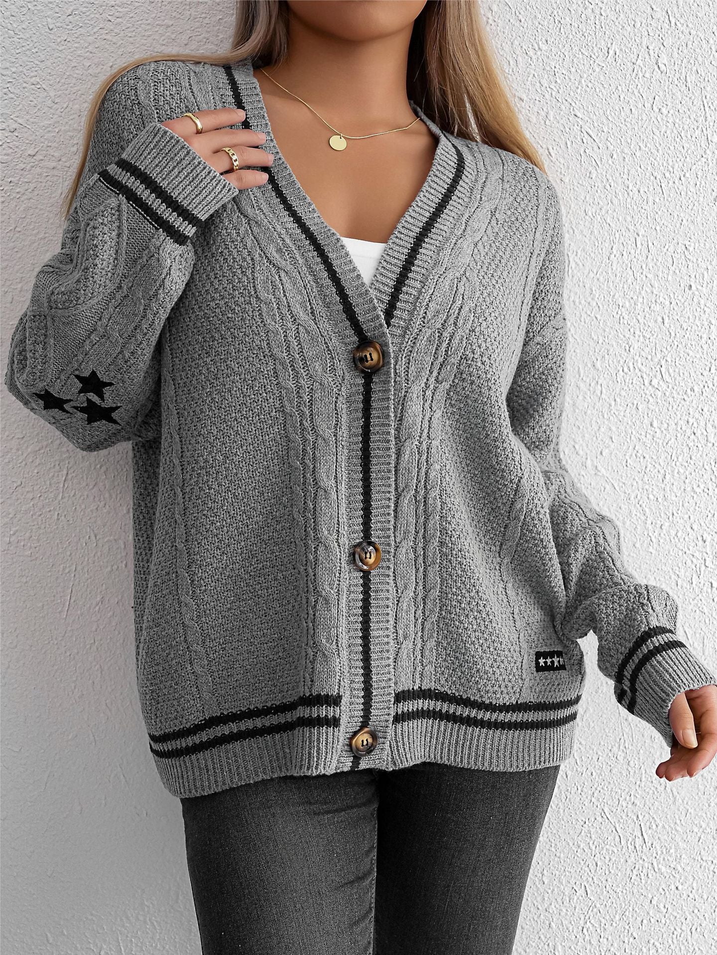 Gray cable knit cardigan with black trim and star accents, paired with dark jeans