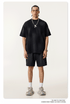 Model in black t-shirt and shorts set with silver chain necklace, white socks against cream background