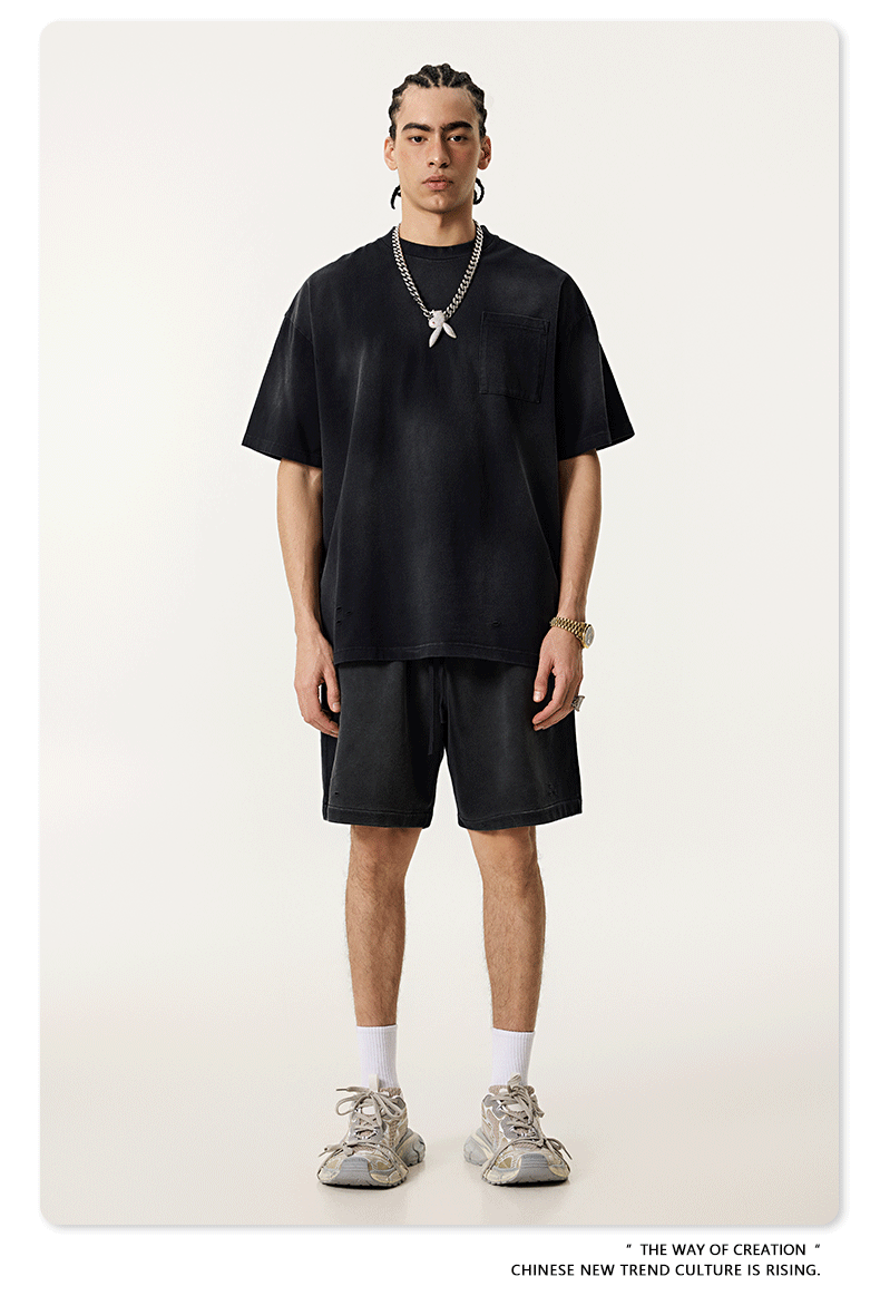 Model in black t-shirt and shorts set with silver chain necklace, white socks against cream background