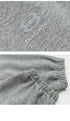 A close-up of the embroidered logo on gray sweatpants, showing the soft fleece texture and elastic cuff detail