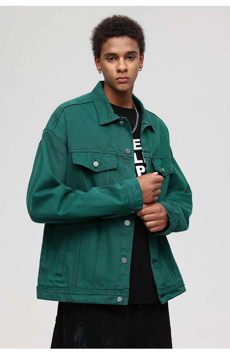 A man modeling forest green denim jacket with silver buttons over black graphic tee with chain necklace against white background