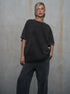 Person wearing a black oversized t-shirt and pants against a gray concrete wall.