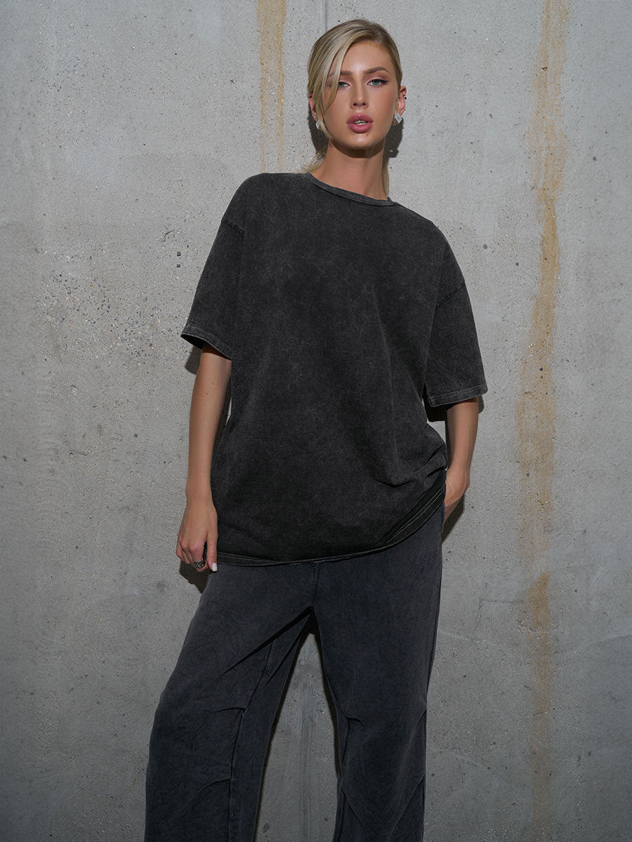Person wearing a black oversized t-shirt and pants against a gray concrete wall.
