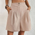 Model wearing khaki pleated shorts with dual button closure and side pockets, paired with white crop top