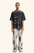 A model wearing black graffiti-print oversized t-shirt and light gray tie-dye pants against white backdrop, silver chain necklace