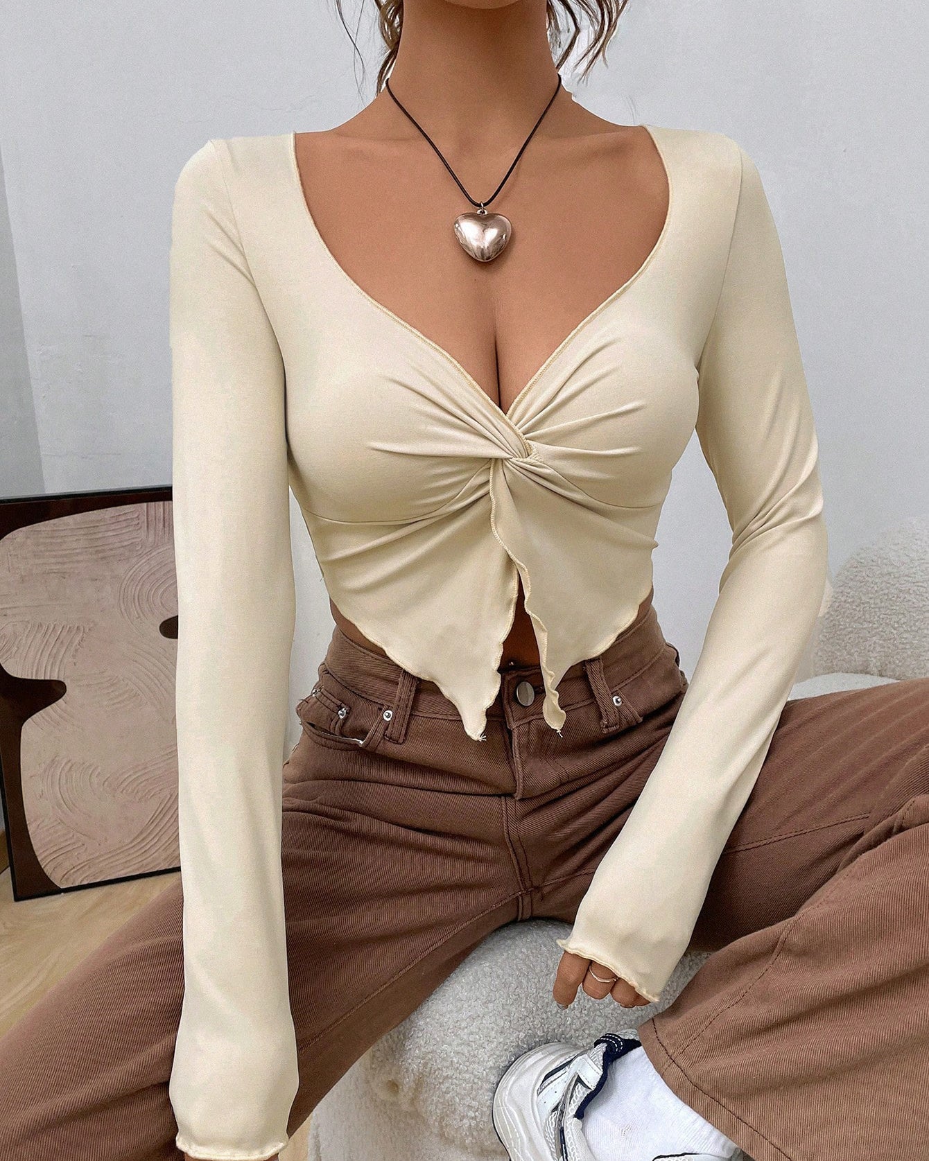 Model wearing cream long-sleeve twist-front crop top with brown jeans, silver heart necklace, and white sneakers